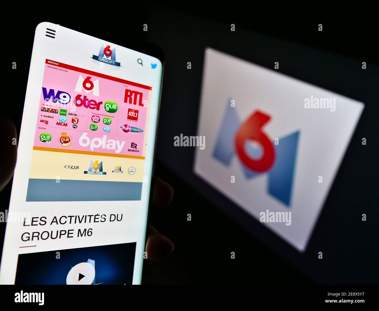 Person, die Mobiltelefon mit der Website des französischen Medienunternehmens Metropole Télévision S.A. (Groupe M6) vor dem Logo hält. Konzentrieren Sie sich auf die Mitte des Telefonbildschirms. Stockfoto