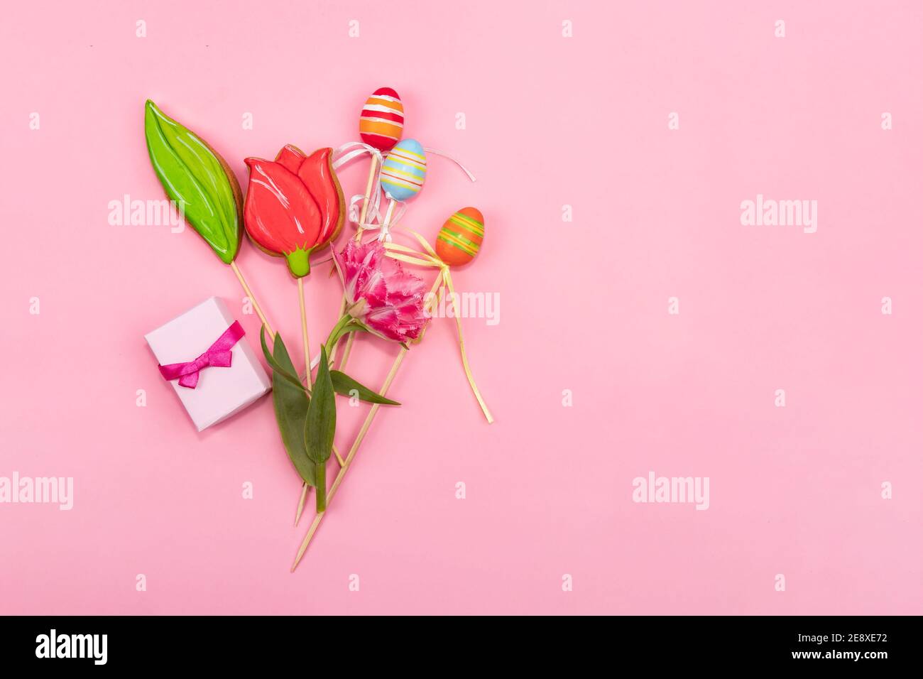 Frühlingskarte Konzept. Ein Strauß Tulpen, Plätzchen in Form einer Tulpe, Ostereier und eine kleine Schachtel mit Gewürzen liegt auf einem rosa Hintergrund. Stockfoto
