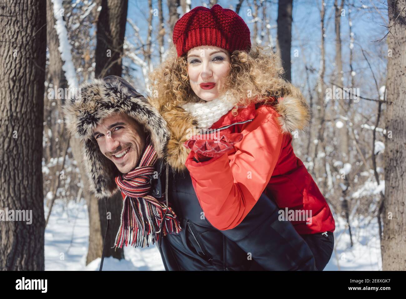 Mann trägt seine Frau Huckepack im Winter, während sie ist Einen Kuss blasen Stockfoto