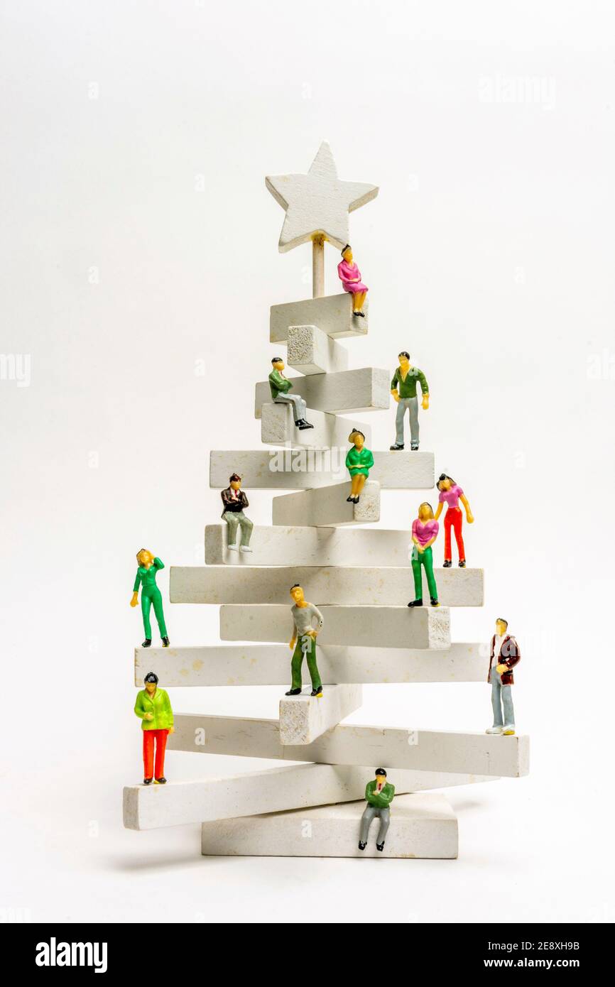 Kreativer Weihnachtsbaum aus Holzblöcken mit Miniaturfiguren, die ihn in bunten Outfits verzieren Stockfoto