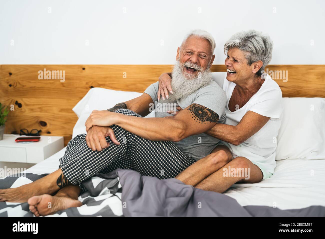 Glückliches Seniorenpaar lächelt zusammen im Bett - Hipster reif Leute, die eine lustige Schlafzeit haben - älterer Lebensstil und Liebe Beziehungskonzept Stockfoto