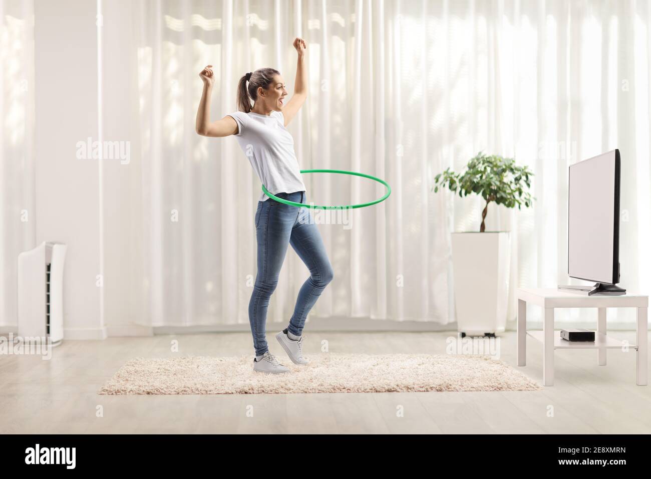 Junge Frau spinnend Hula Hoop zu Hause in einem Leben Zimmer vor dem fernseher Stockfoto