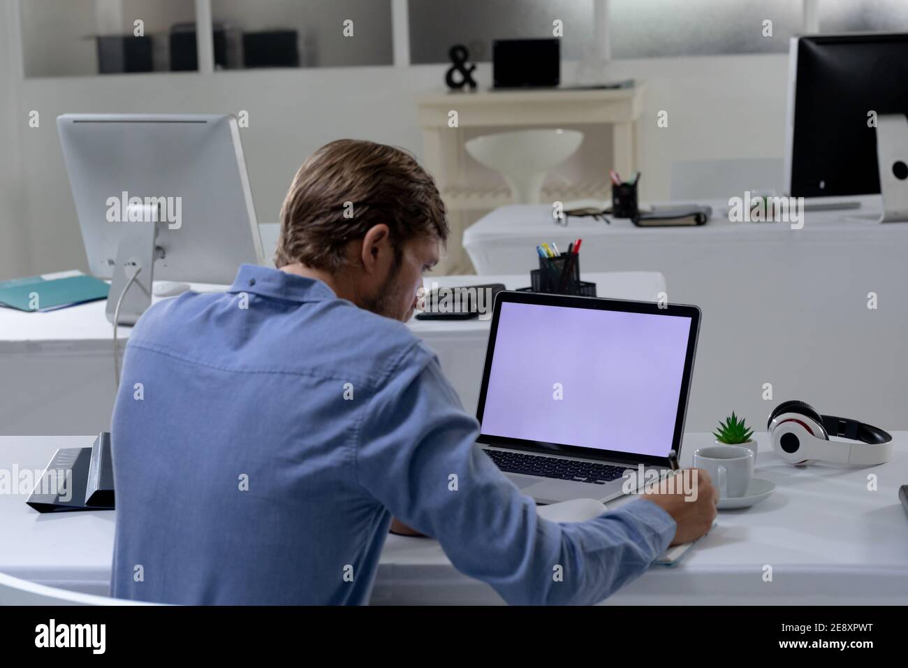 Kaukasischer Geschäftsmann sitzt am Schreibtisch mit Laptop in einem leeren Büro Stockfoto