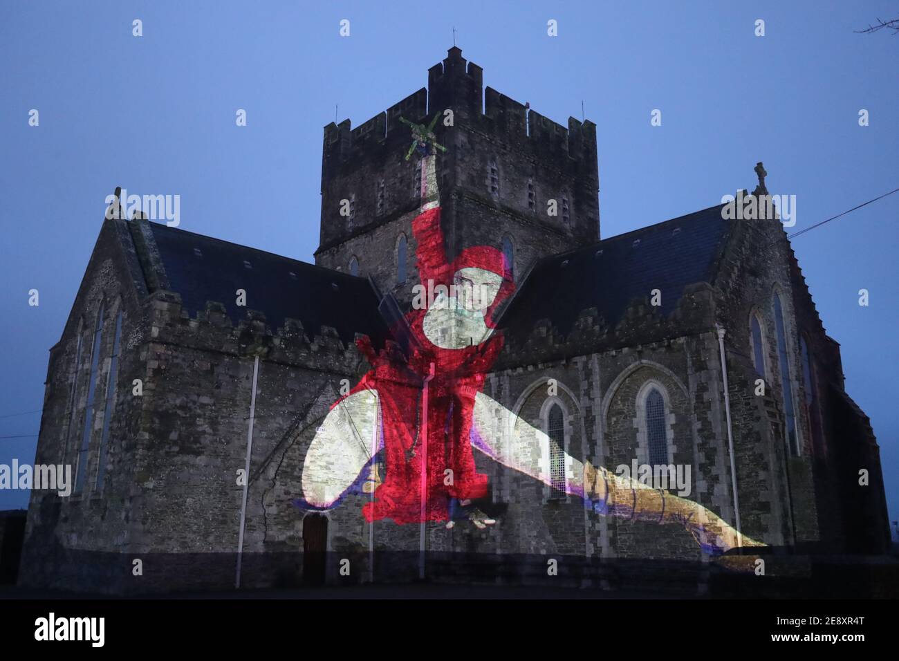 Eine Nonne in Rot mit einem Kruzifix, das im Rahmen der Herstory Light Show auf der St. Brigid's Cathedral, Kildare, am St. BrigidÕs Day projiziert wird, als Wahrzeichen in ganz Irland beleuchtet wurden, um Überlebende von Mutter- und Babyhäusern zu ehren, als Teil einer Veranstaltung zum St. Brigid's Day. Bilddatum: Montag, 1. Februar 2021. Stockfoto