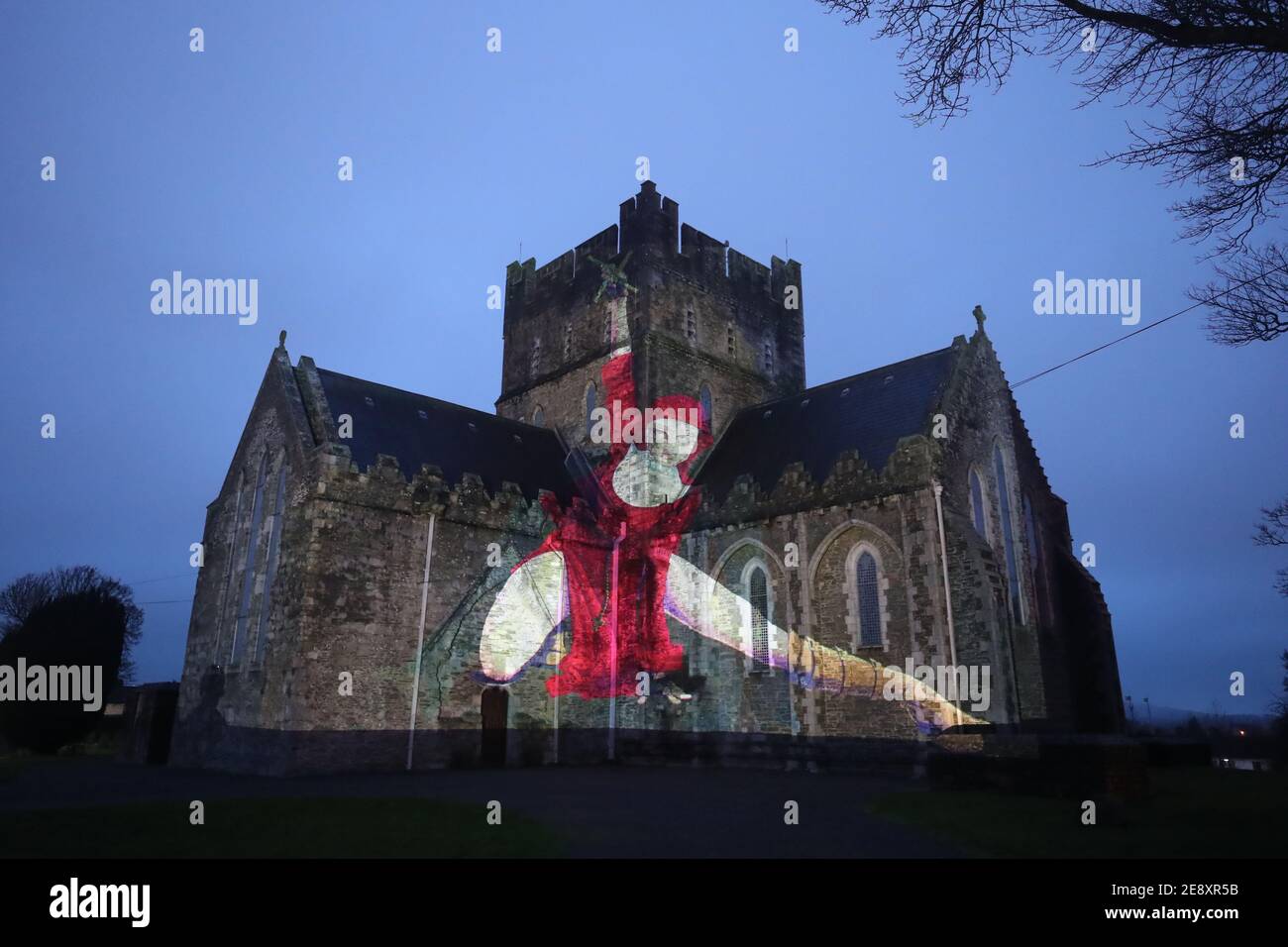 Eine Nonne in Rot mit einem Kruzifix, das im Rahmen der Herstory Light Show auf der St. Brigid's Cathedral, Kildare, am St. Brigid's Day projiziert wird, wenn Wahrzeichen in ganz Irland beleuchtet wurden, um Überlebende von Mutter- und Babyhäusern zu ehren, als Teil einer Veranstaltung zum St. Brigid's Day. Bilddatum: Montag, 1. Februar 2021. Stockfoto