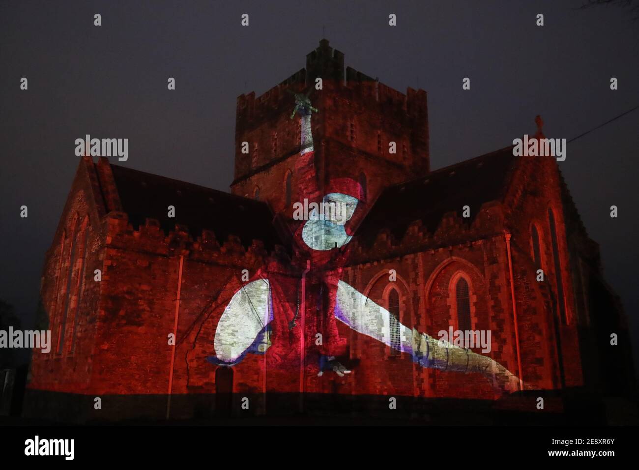 Eine Nonne in Rot mit einem Kruzifix, das im Rahmen der Herstory Light Show auf der St. Brigid's Cathedral, Kildare, am St. BrigidÕs Day projiziert wird, als Wahrzeichen in ganz Irland beleuchtet wurden, um Überlebende von Mutter- und Babyhäusern zu ehren, als Teil einer Veranstaltung zum St. Brigid's Day. Bilddatum: Montag, 1. Februar 2021. Stockfoto