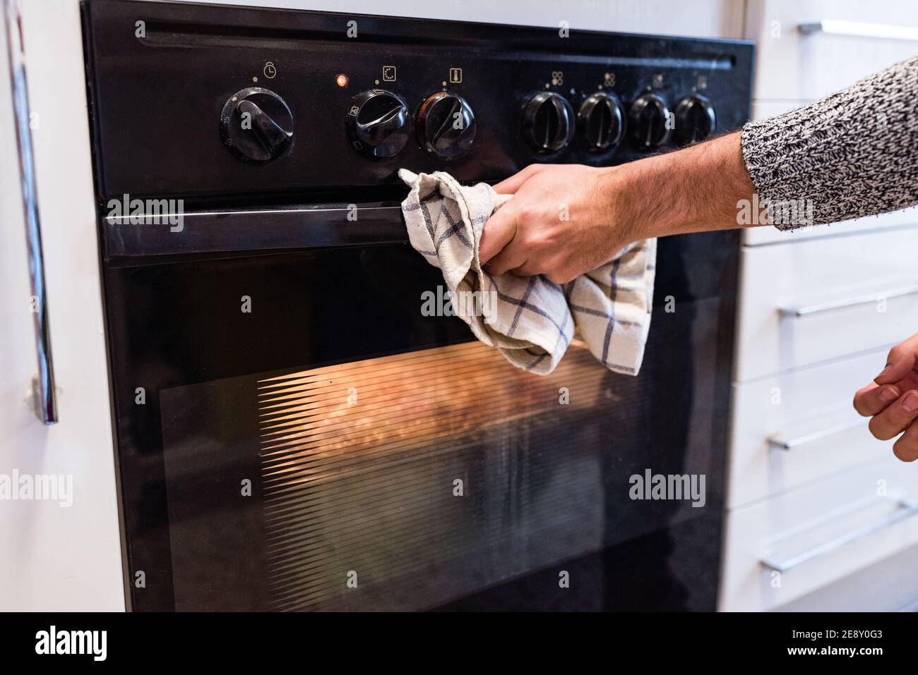 Mann hält ein Küchentuch mit den Händen zu vermeiden Beim Öffnen eines beleuchteten Backofens verbrannt werden Stockfoto