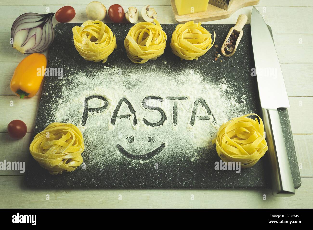 Hausgemachte Eiernudeln auf dem Tisch als Hintergrund mit Platz für Text. Das Wort Pasta wird mit dem Finger auf das Mehl geschrieben. Makkaroni mit Tomaten Stockfoto