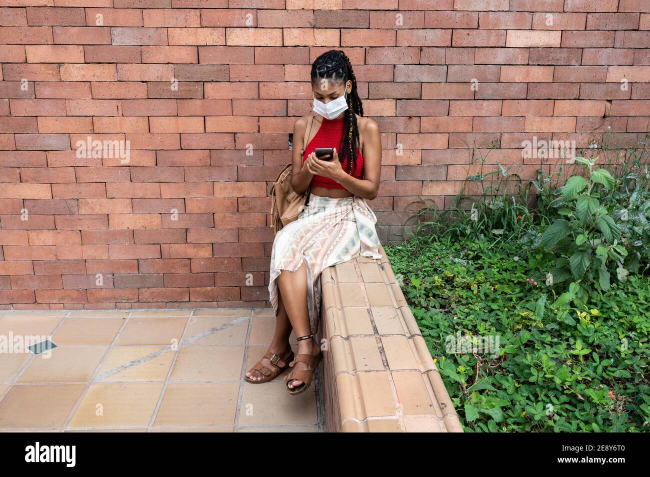Junge afro latina Frau in Gesichtsmaske mit ihrem Smartphone in der Straße, Kolumbien Stockfoto