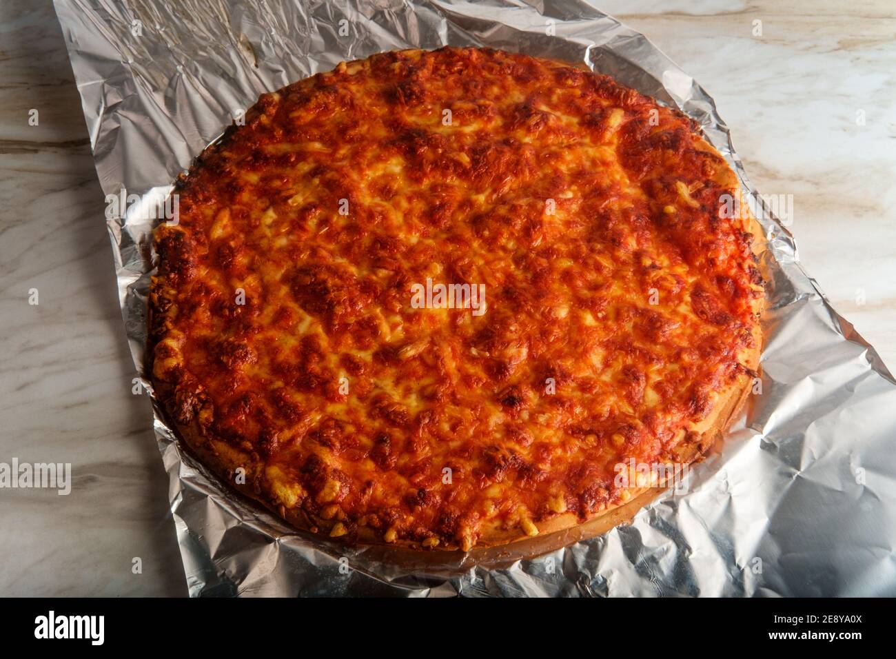 Ungeschnittener knuspriger Pizzakuchen im NYC-Stil auf Blechfolie Stockfoto