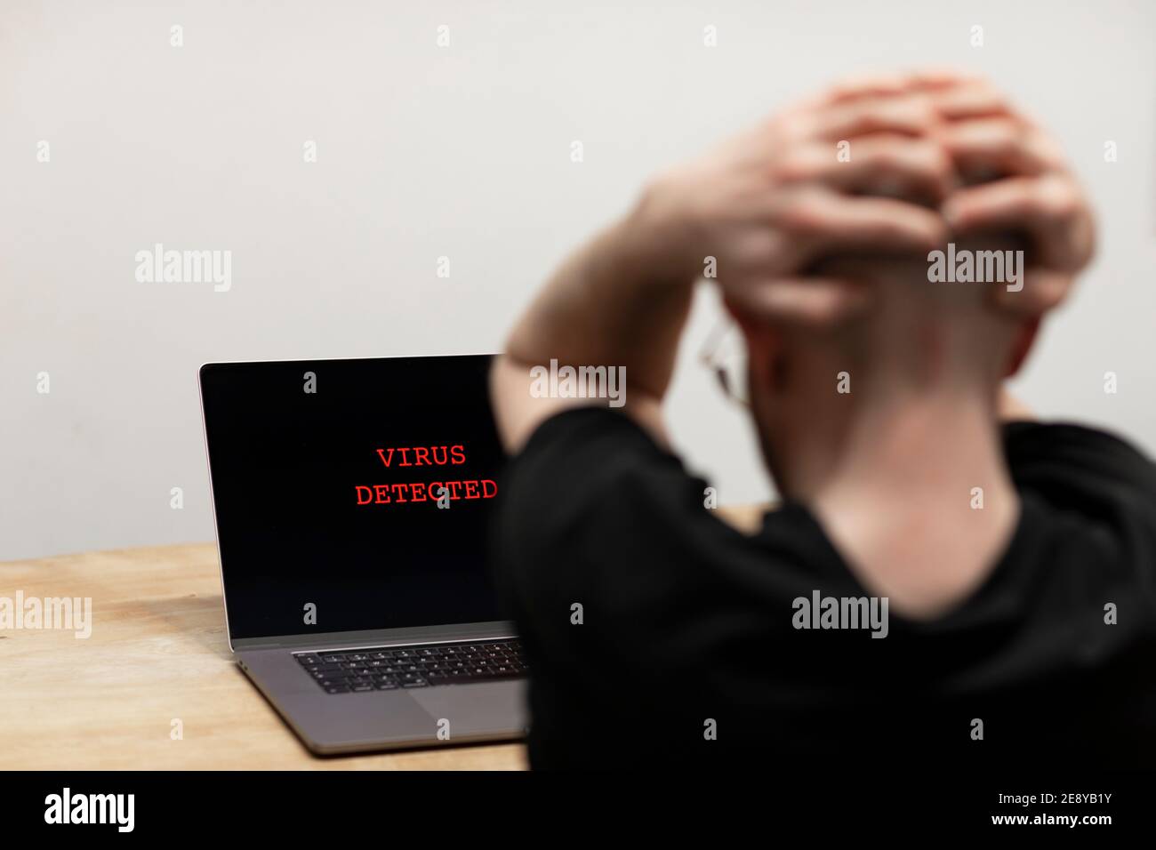 Auf einem Laptop wurde ein Virus entdeckt. Ein verzweifelter Mann, der seinen Computer mit der Warnung auf seinem Bildschirm betrachtet. Cyberkriminalität, infiziertes unsicheres Gerät Stockfoto