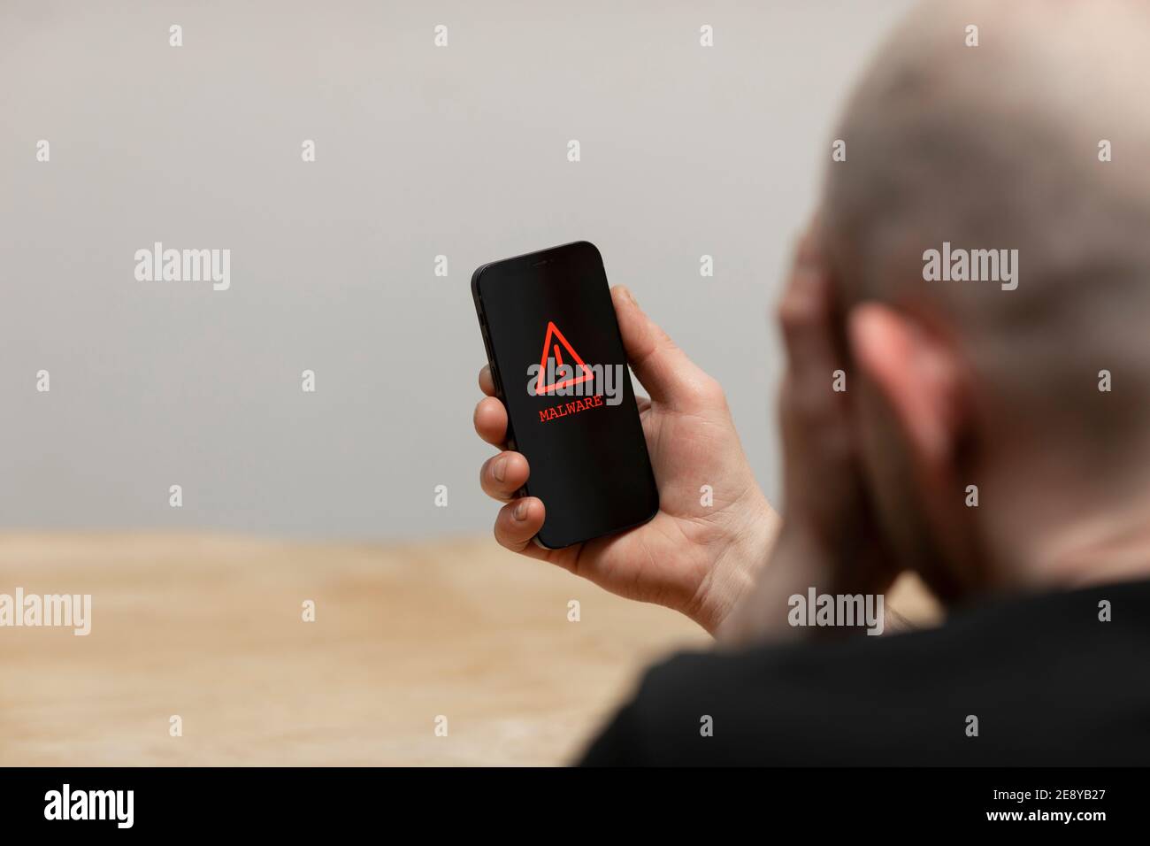 Ein Malware-Text und ein Warnschild, das auf einem Handy-Bildschirm erscheint. Ein verzweifelter Mann hält sein gehacktes infiziertes Telefon. Stockfoto