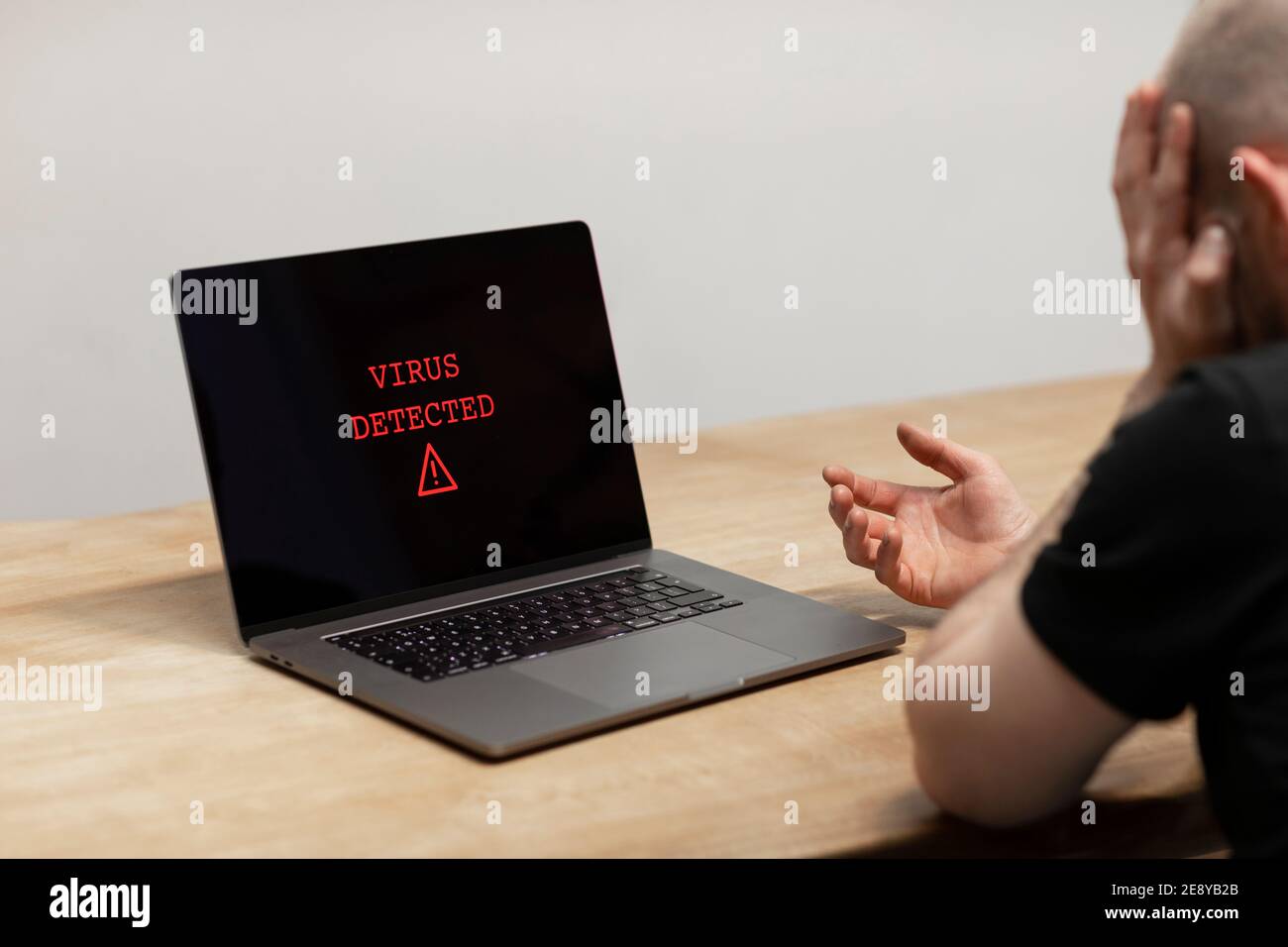 Auf einem Laptop wurde ein Virus entdeckt. Ein verzweifelter Mann sitzt vor seinem Computer mit der Warnung auf seinem Bildschirm. Cyberkriminalität, infiziertes unsicheres Gerät Stockfoto