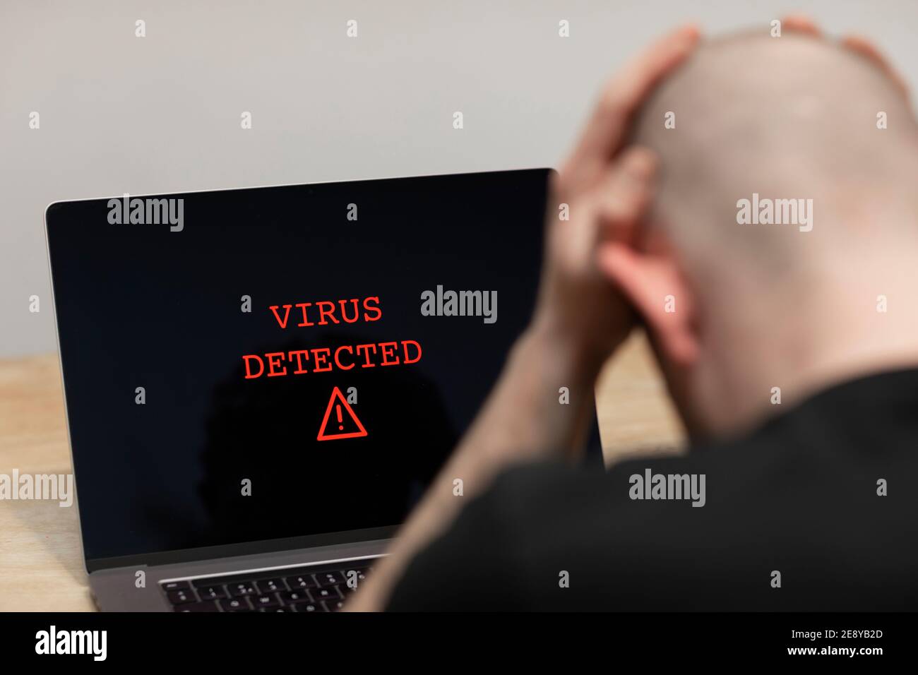 Ein Virus wurde mit einem Warnzeichen auf einem Laptop erkannt. Ein verzweifelter Mann sitzt vor seinem Computer mit der Warnung auf seinem Bildschirm. Cyberkriminalität, infiziert Stockfoto