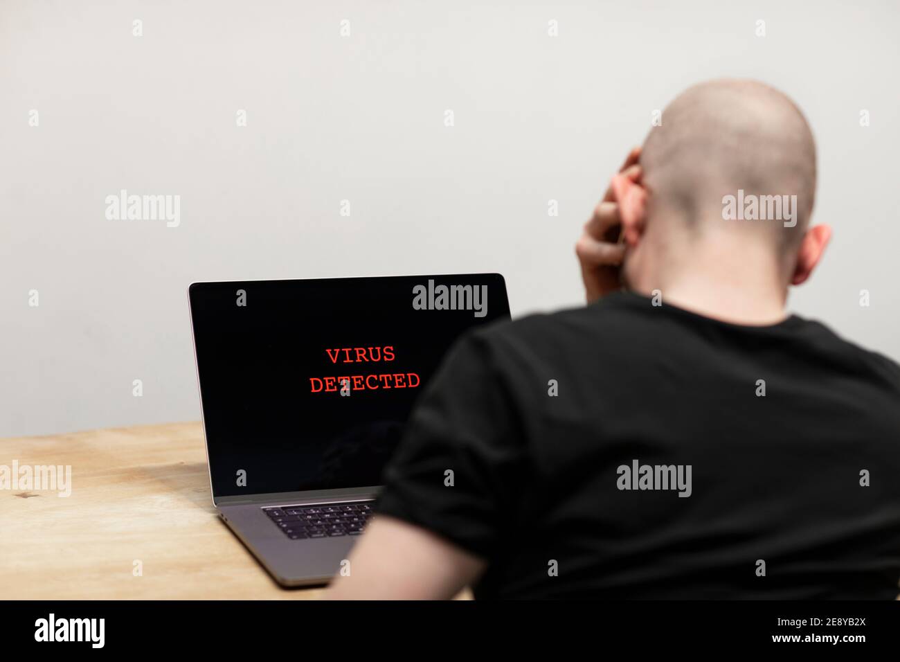 Virus erkannt und ein Warnzeichen rot auf einem Laptop angezeigt. Ein verzweifelter Mann sitzt vor seinem Computer looking auf den Text auf seinem Bildschirm. Cyberkriminalität, Stockfoto
