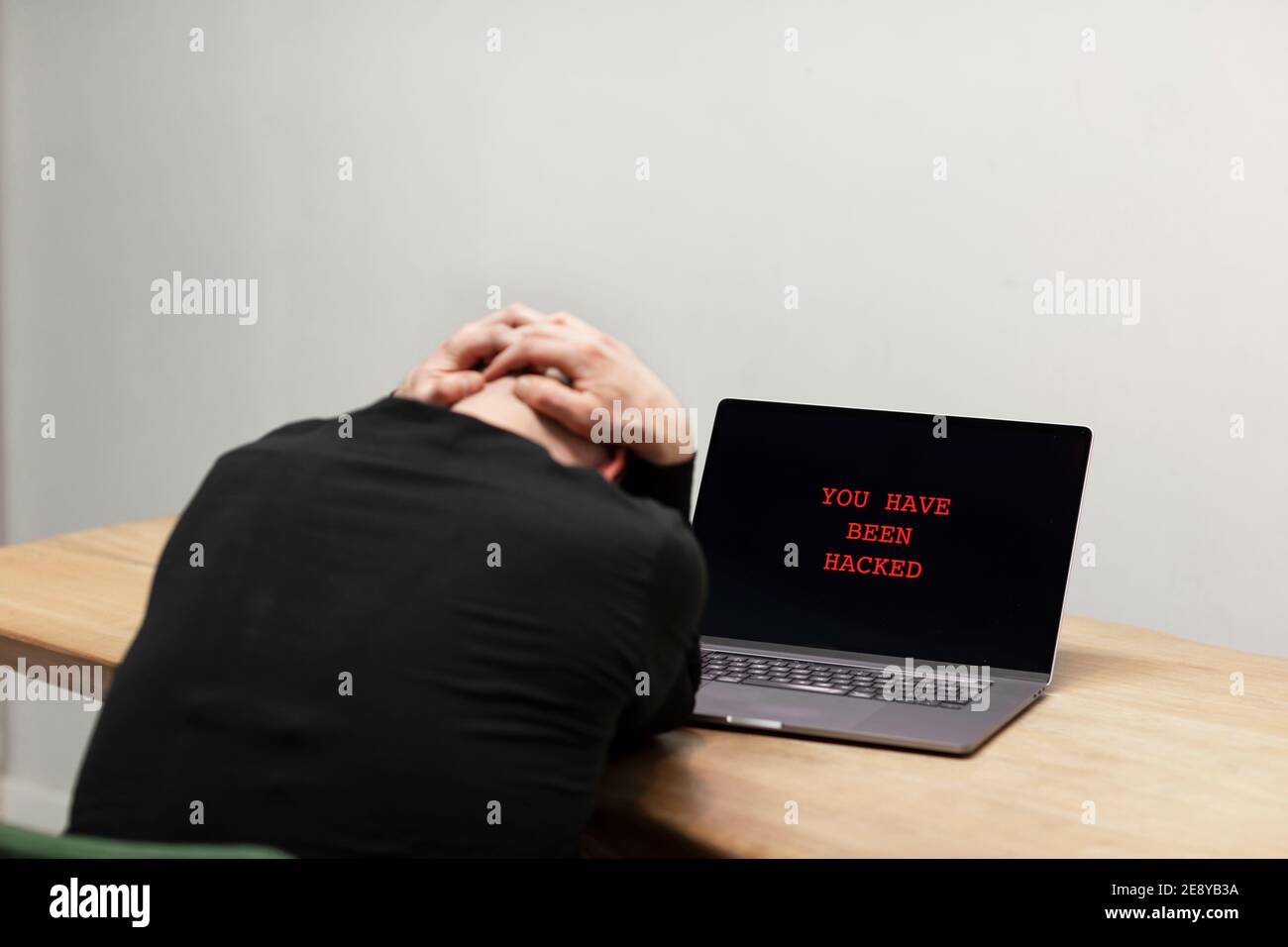 Roter Text auf einem Laptop, der sagt ‘Sie wurden gehackt’. Ein verzweifelter trauriger Mann, der vor seinem infizierten Computer sitzt. Cyberkriminalität, infiziertes unsicheres Gerät Stockfoto