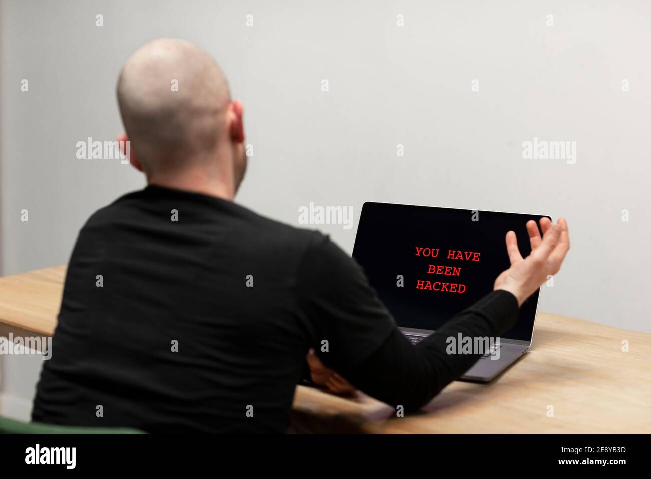Roter Text auf einem Laptop, der sagt ‘Sie wurden gehackt’. Ein verzweifelter irritierter Mann, der vor seinem infizierten Computer sitzt. Cyberkriminalität, infizierte unsichere d Stockfoto