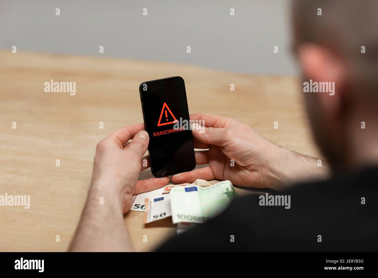 Ransomware Text und rote Warnzeichen auftauchen auf einem Handy-Bildschirm. Ein verzweifelter Mann, der sein gehacktes infiziertes Telefon hielt, bereit, seine Erpressung zu bezahlen Stockfoto