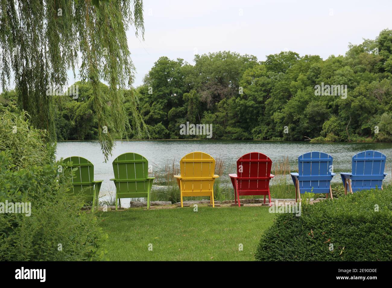 Sechs bunte Holzstühle an einem Seeufer umgeben von Wald in Janesville, Wisconsin, USA Stockfoto