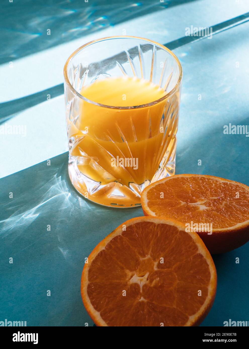 Glas frisch gepressten Orangensaft isoliert auf türkisblau Hintergrund und Sonnenstrahlen Stockfoto