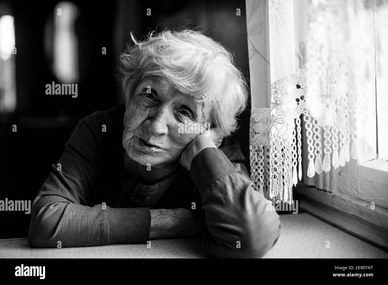 Die alte Dame sitzt am Küchentisch. Schwarzweiß-Foto. Stockfoto