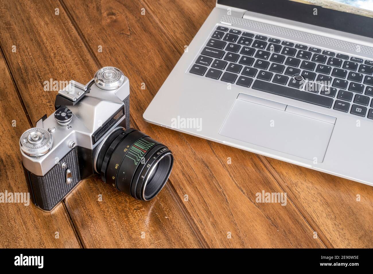 Eine alte 35 mm Spiegelreflexkamera auf einem Holztisch neben einem modernen Laptop, ein Kontrast zwischen modern und alt, horinzontal Stockfoto