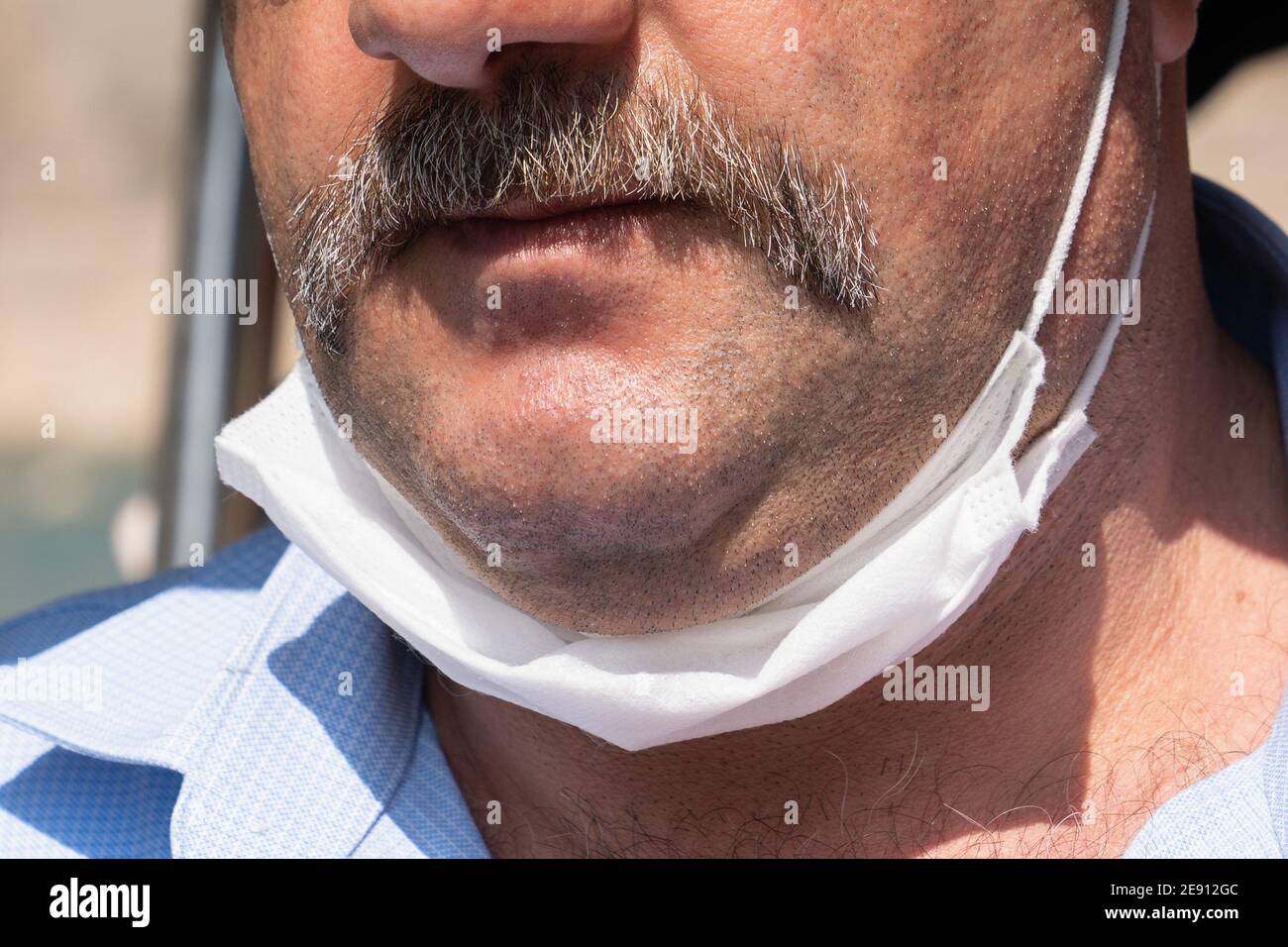 Schnurrbart Mann mit einer weißen schützenden medizinischen Maske, bis zum Kinn gesenkt. Falsches Tragen von medizinischen Masken unter Quarantäne. Nahaufnahme. Stockfoto