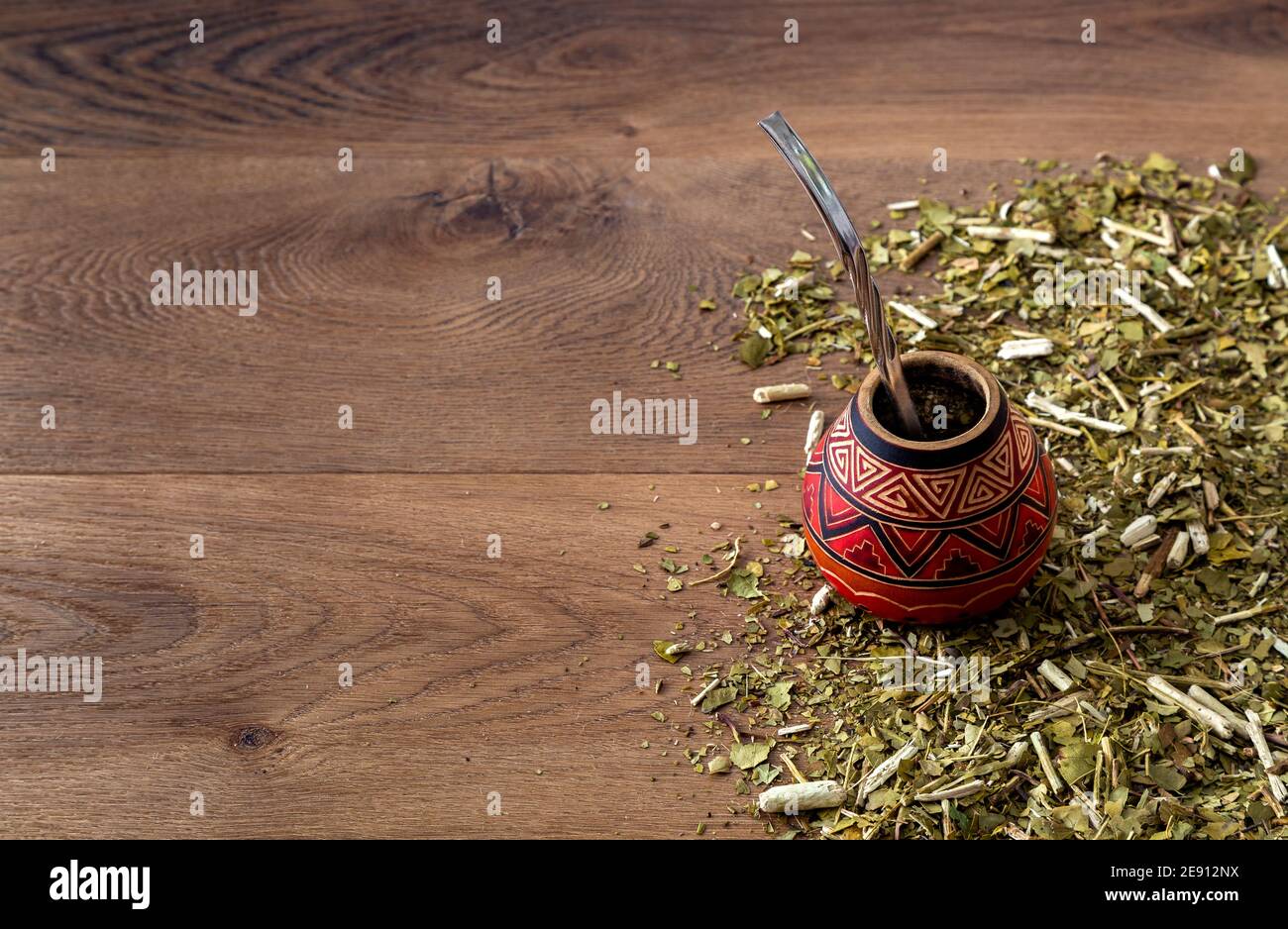 Traditionelle Mate aus Kalabash über einem Holztisch mit Yerba Mate darüber verstreut. Stockfoto