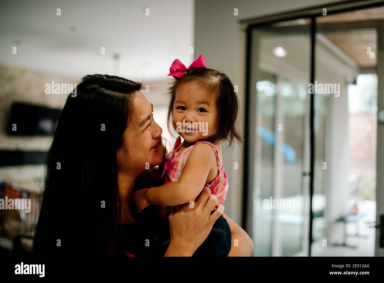 Glücklich Mutter halten junge lächelnd asiatische Tochter mit Bogen im Haare Stockfoto