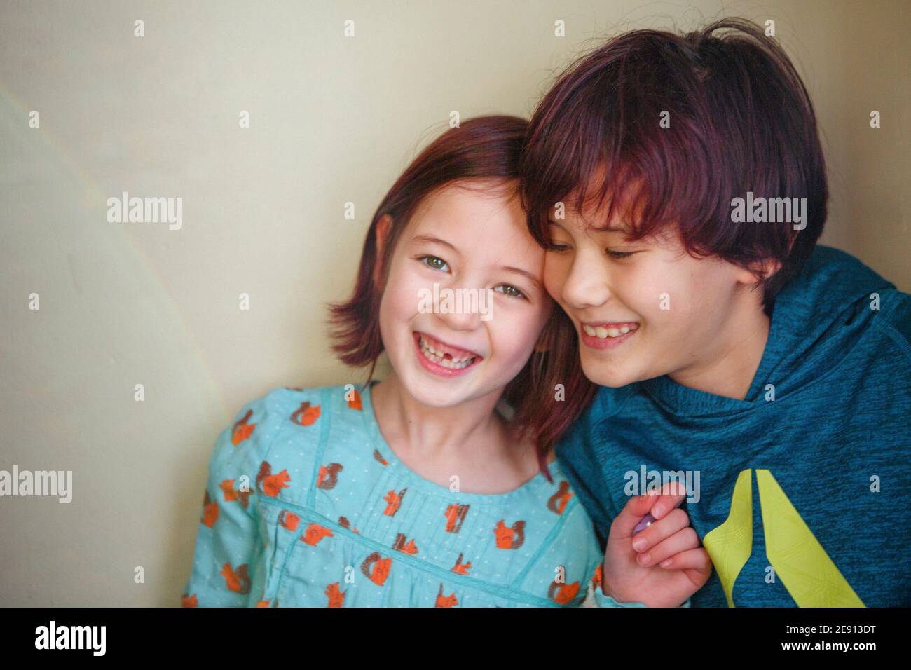 Zwei glückliche, lächelnde Kinder lehnen sich dicht an eine Wand Stockfoto