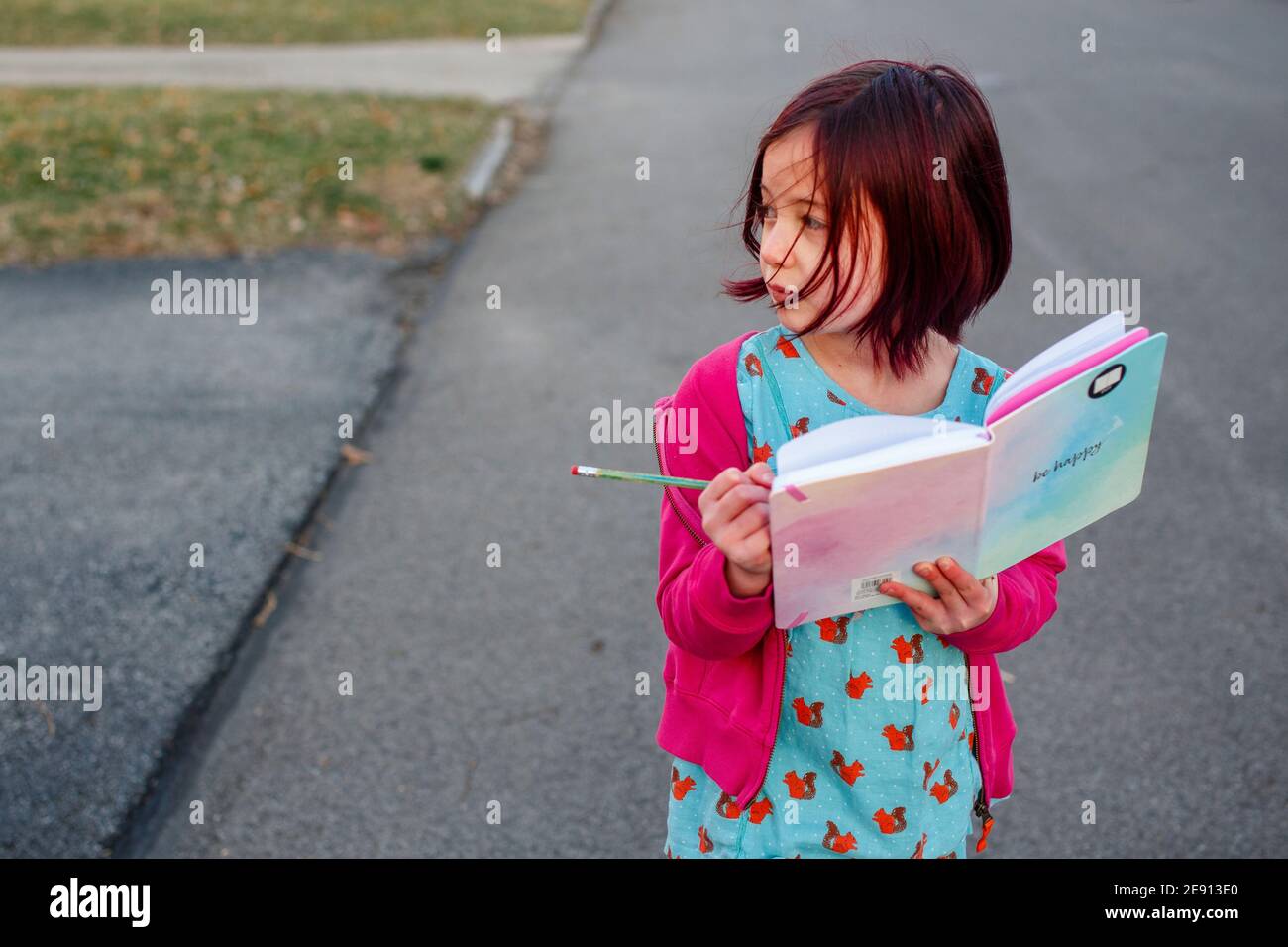 Ein windgeblasenes kleines Mädchen geht die Straße hinunter und notiert sich Ein Journal Stockfoto