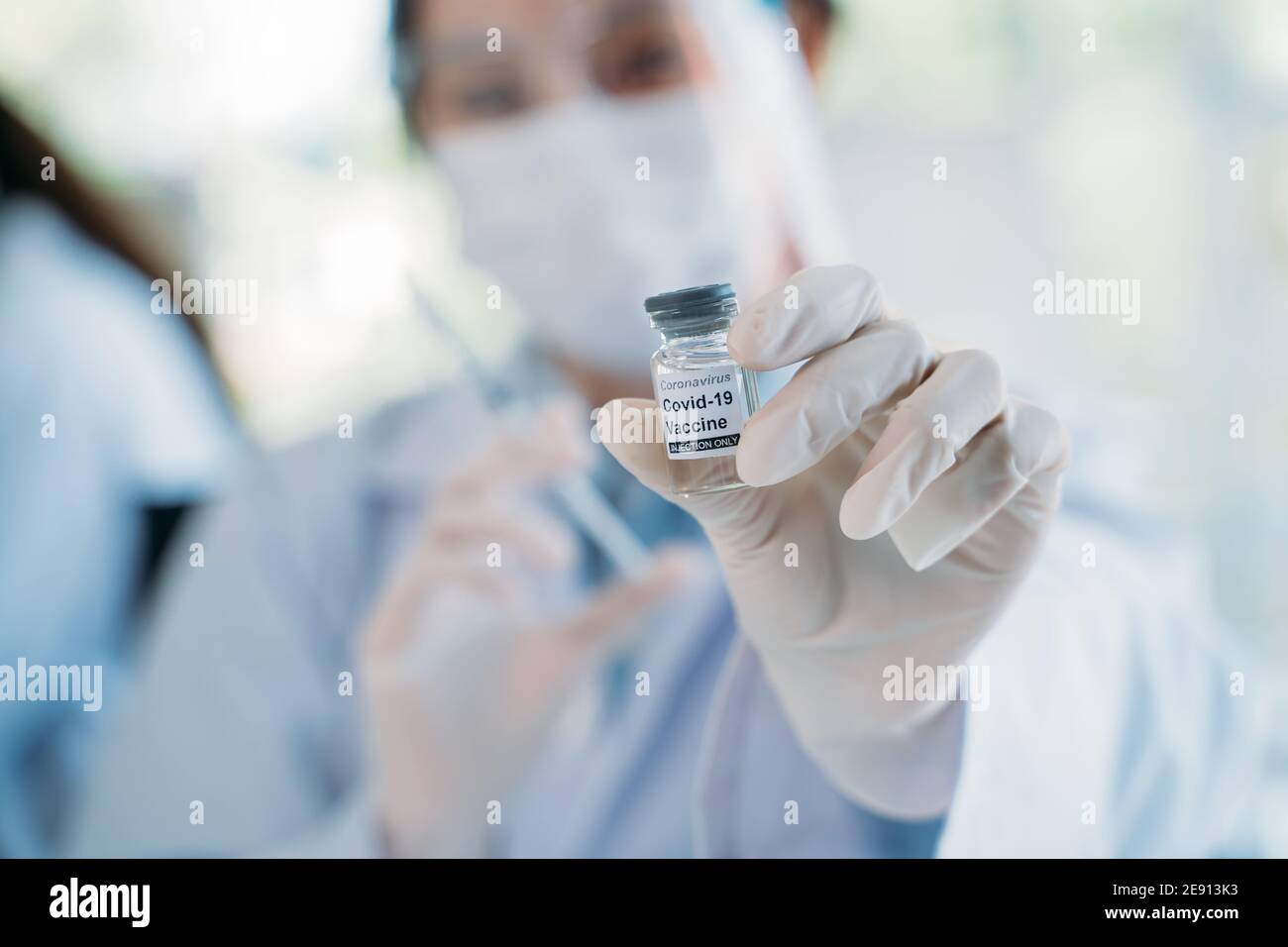Ärztin mit chirurgischer Gesichtsmaske und Gesichtsschutz mit Spritze mit Nadel und COVID-19 Coronavirus-Impfstoffröhrchen mit Kopierraum. Healthcare und Medizin Konzept Stockfoto
