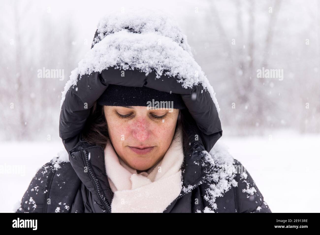 Friedliche Frau in warmer Jacke mit Schnee im Stehen bedeckt Wald im Winter bei Schneefall in Pemberton und Blick nach unten Stockfoto