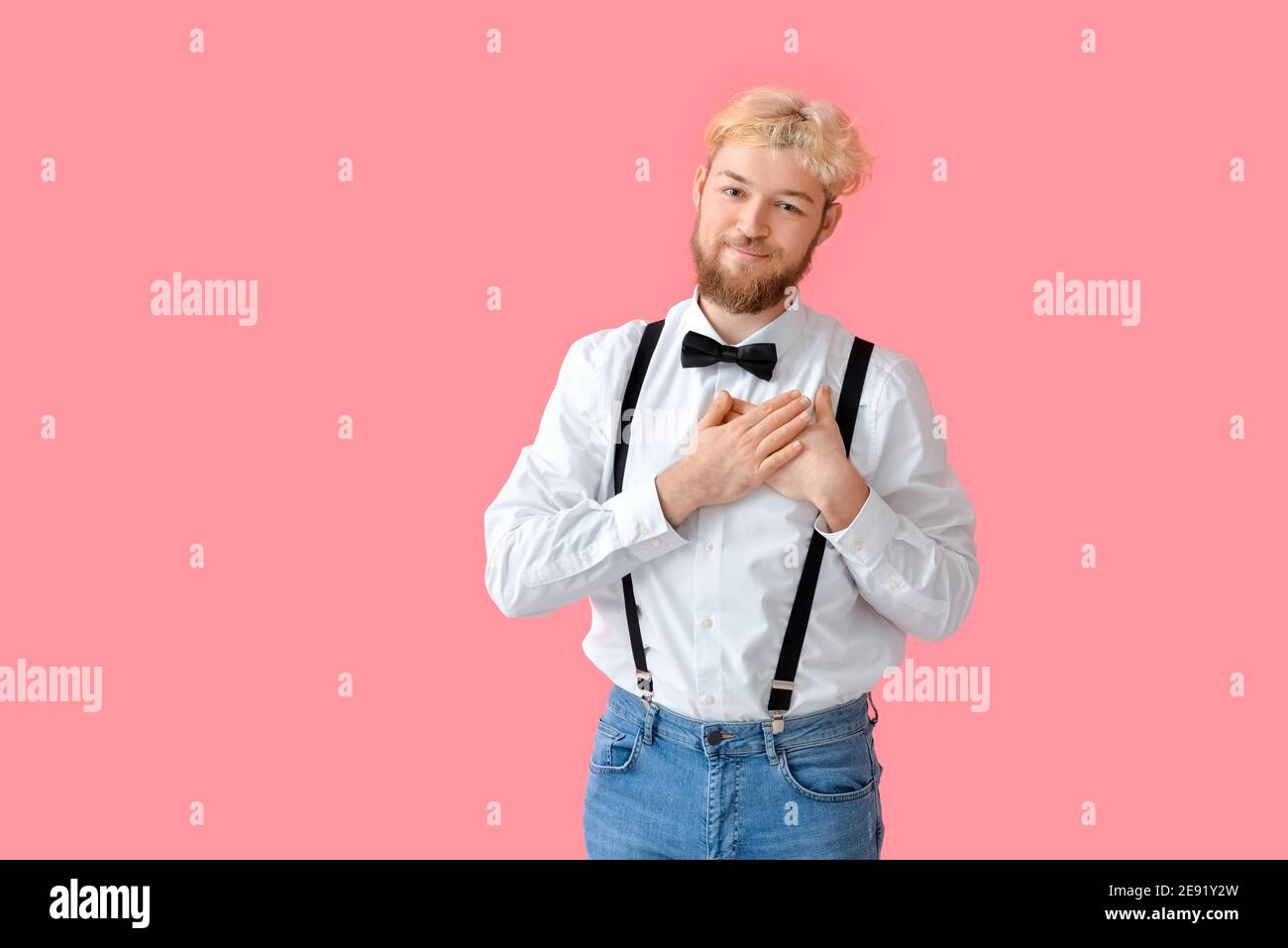 Schöner junger Mann, der die Hände gegen die Farbe auf sein Herz legt Hintergrund Stockfoto