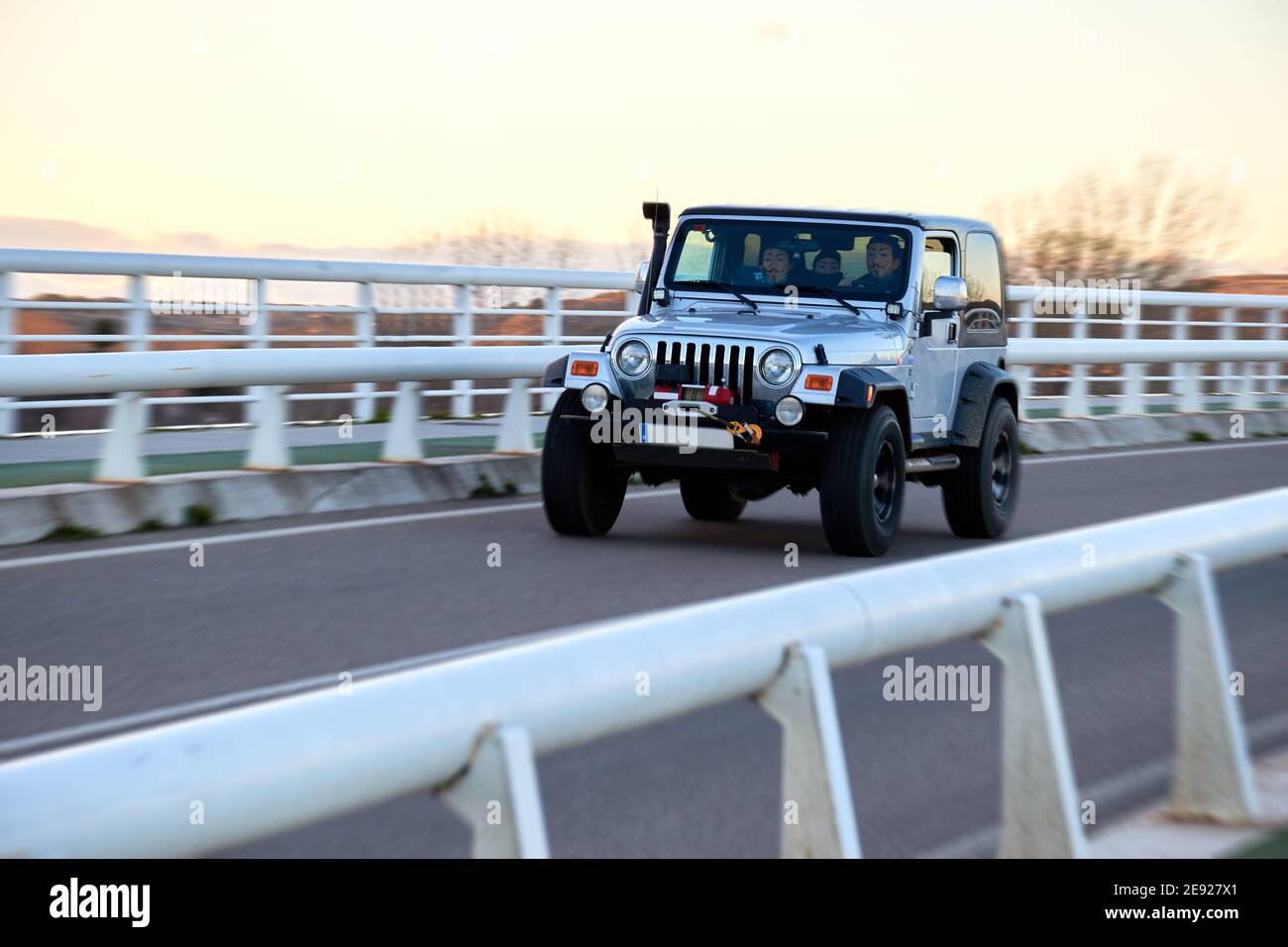 Jeep Wrangler rubicon über eine Brücke bei Sonnenuntergang, Tapete. Off-Road vorbereitet Off-Road Jeep in silberner Farbe, Esche, 3 Personen mit einer Maske. Nicht Erkannt Stockfoto