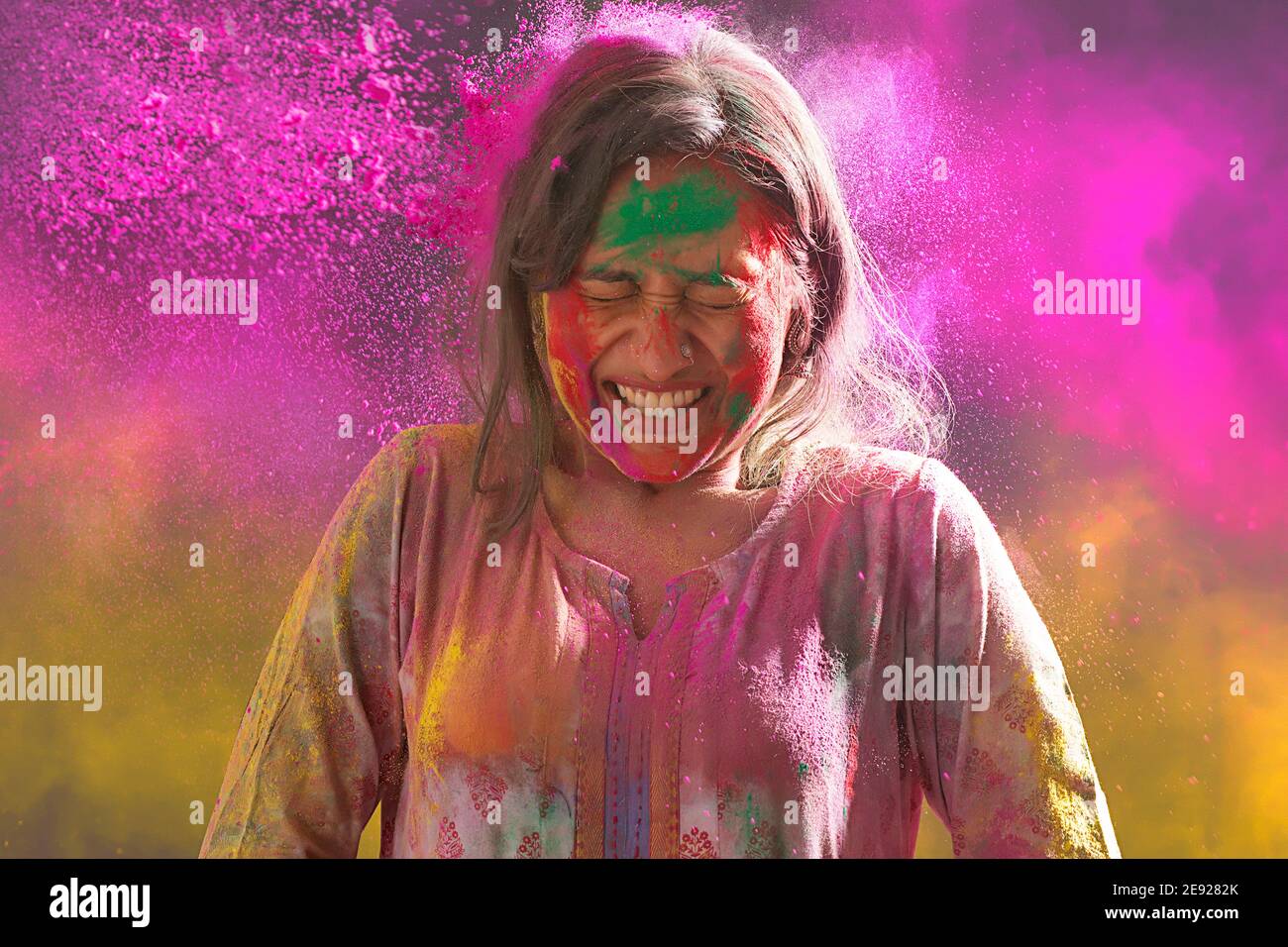 Frau lächelt ekstatisch beim Spielen mit Farben auf Holi Stockfoto