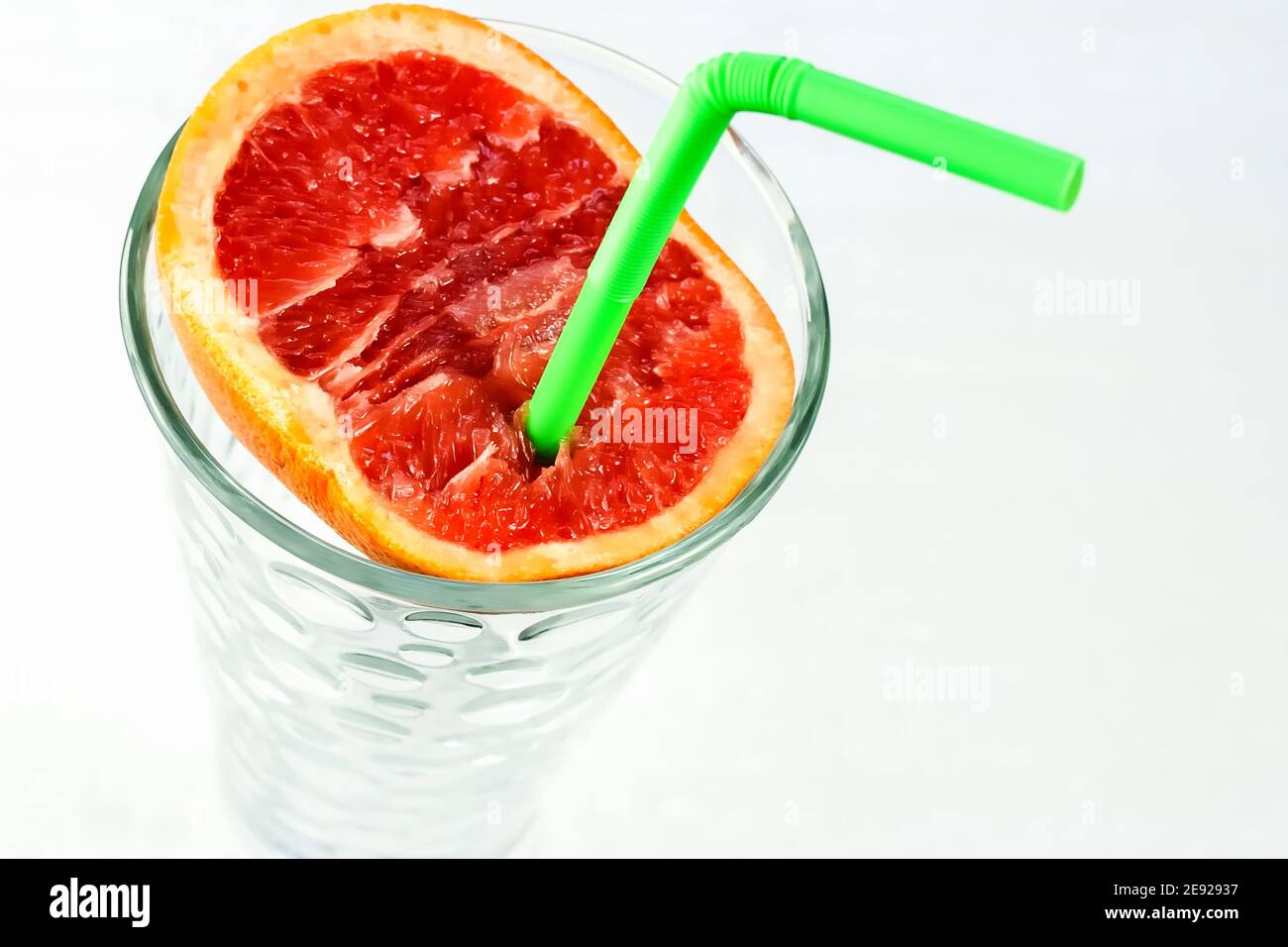 Eine halbe saftige Grapefruit mit einem grünen Trinkhalm im Glas. Ein gesundes und schmackhaftes Zitrusgetränk, das höchste Vitamine enthält. Stockfoto