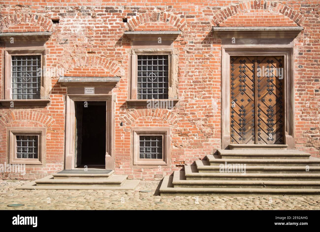 Mauer eines alten roten Backsteingebäudes mit einem geschmiedeten Tür und vier Fenster, auf denen ein gemusterter Schutzgitter Stockfoto