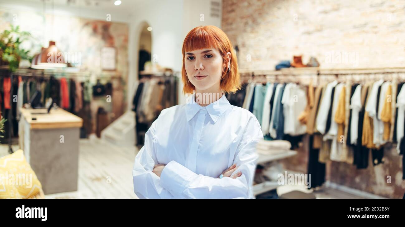 Porträt einer Geschäftsfrau, die mit gekreuzten Armen in ihrer Boutique steht. Modische Frau in ihrem Einzelhandelsgeschäft Kleidung Blick auf Kamera. Stockfoto