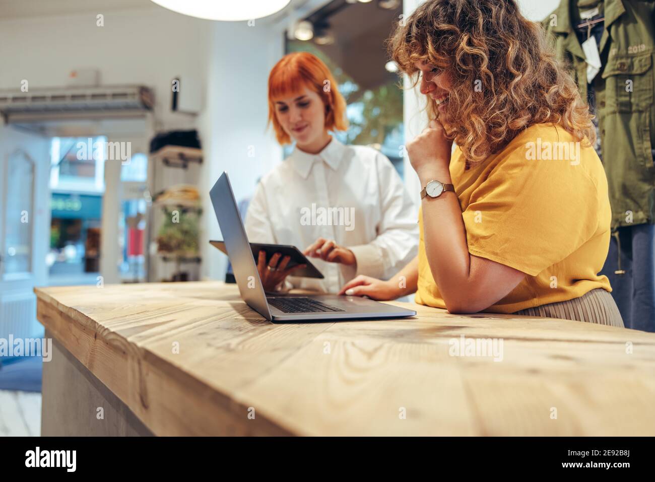 Zwei Frauen, die in einem Bekleidungsgeschäft mit Laptop und digitalem Tablet arbeiten. Mode-Boutique-Besitzer laufen ihr Geschäft online. Stockfoto