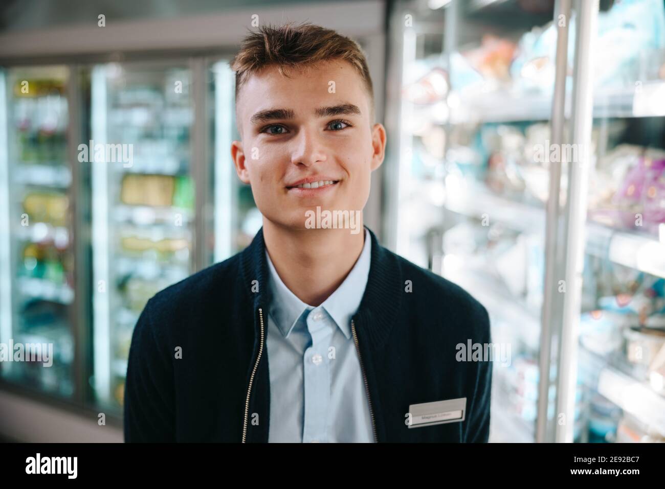 Junger Verkäufer im modernen Supermarkt. Mann auf einem Ferienjob im Lebensmittelgeschäft lächelt an der Kamera. Stockfoto