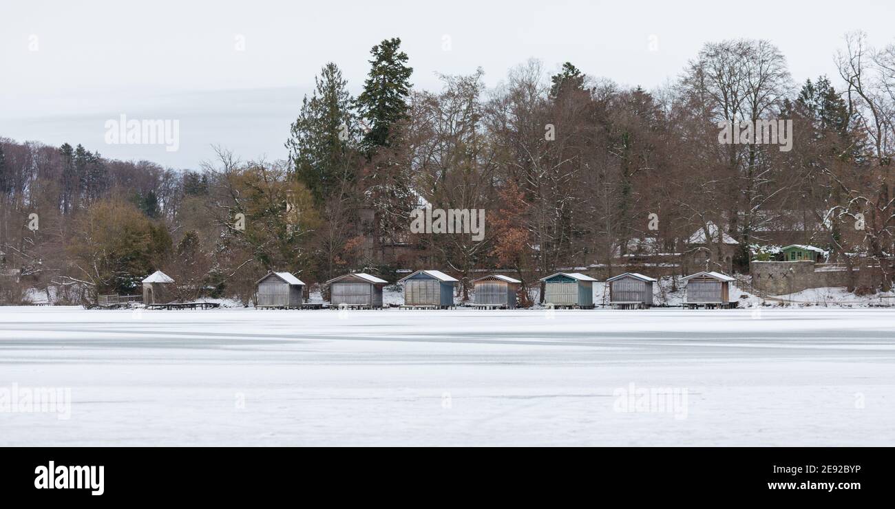 Weßling, Deutschland - 12. Jan 2021: Winterlandschaft mit einem gefrorenen See (Weßlinger See), hölzernen Bootshäusern und Bäumen. Panorama-Format. Stockfoto