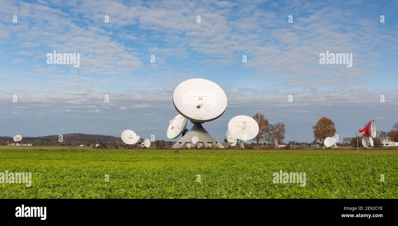 Raisting, Deutschland - 13. Nov 2020: Satellitenschüsseln des Raisting Radome. Mit einem grünen Feld im Vordergrund. Blauer Himmel mit Wolken. Panorama-Format. Stockfoto