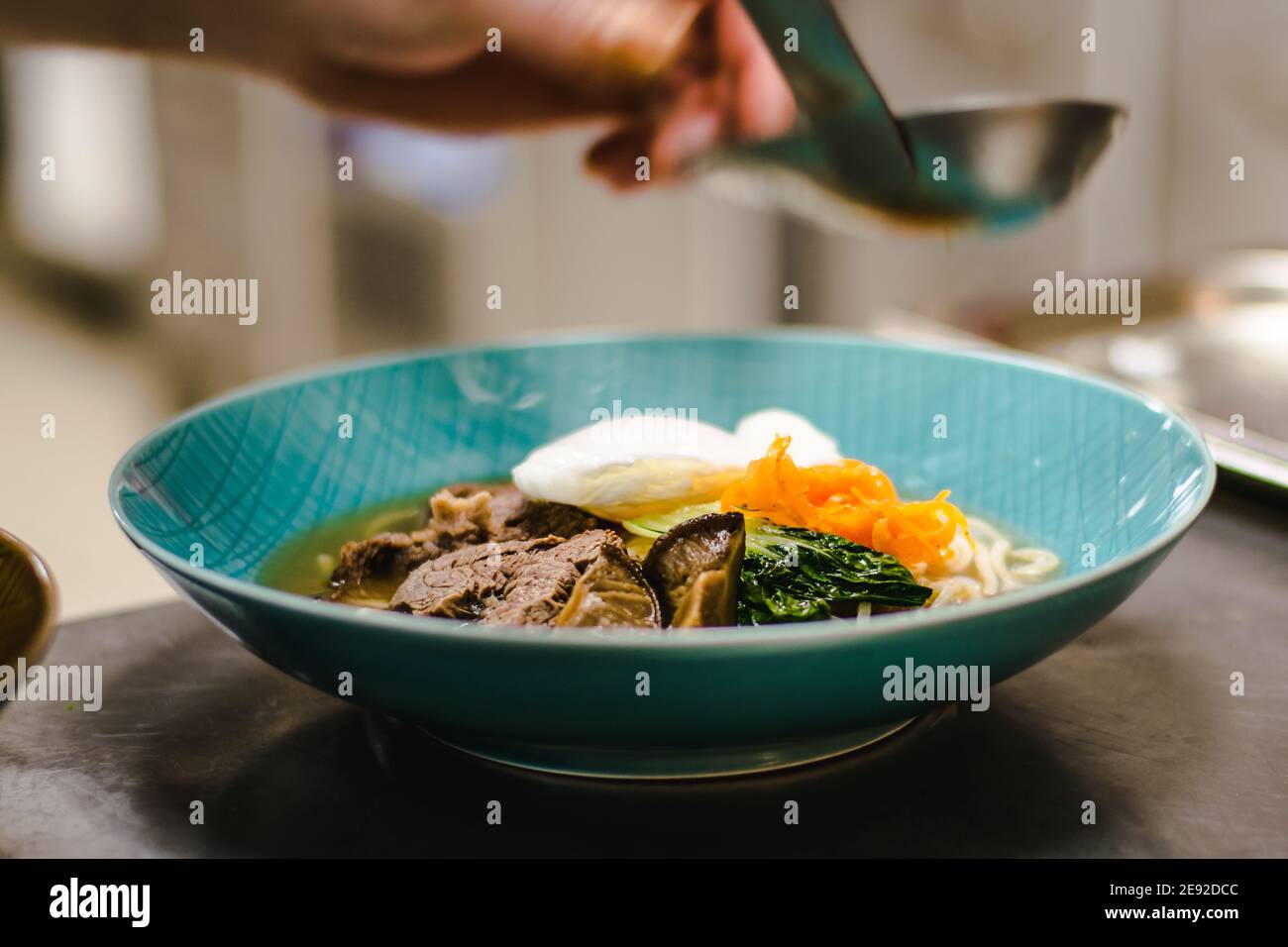 Küchenchef bereitet Ramen-Nudelsuppe mit Fleisch, Eiern und Gemüse in einem Restaurant zu Stockfoto
