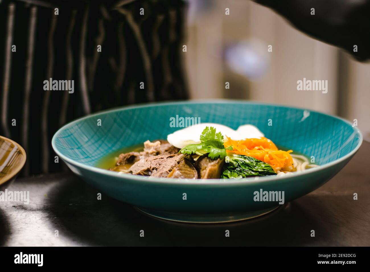 Küchenchef bereitet Ramen-Nudelsuppe mit Fleisch, Eiern und Gemüse in einem Restaurant zu Stockfoto