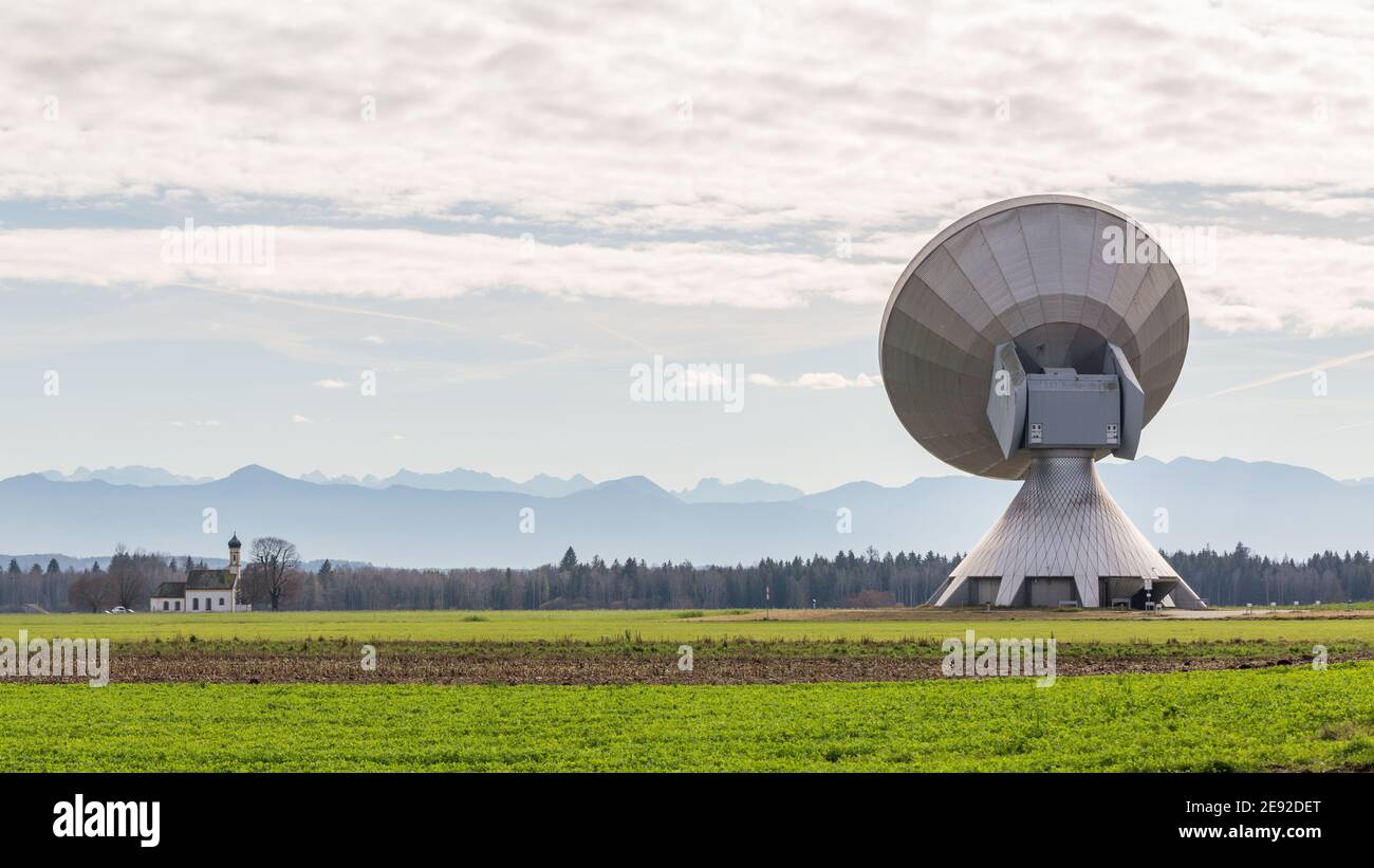 Raisting, Deutschland - 13. Nov 2020: Rückansicht auf einer Satellitenschüssel. In der Ferne die Silhouette der Berge (alpen) und eine Kirche. Stockfoto