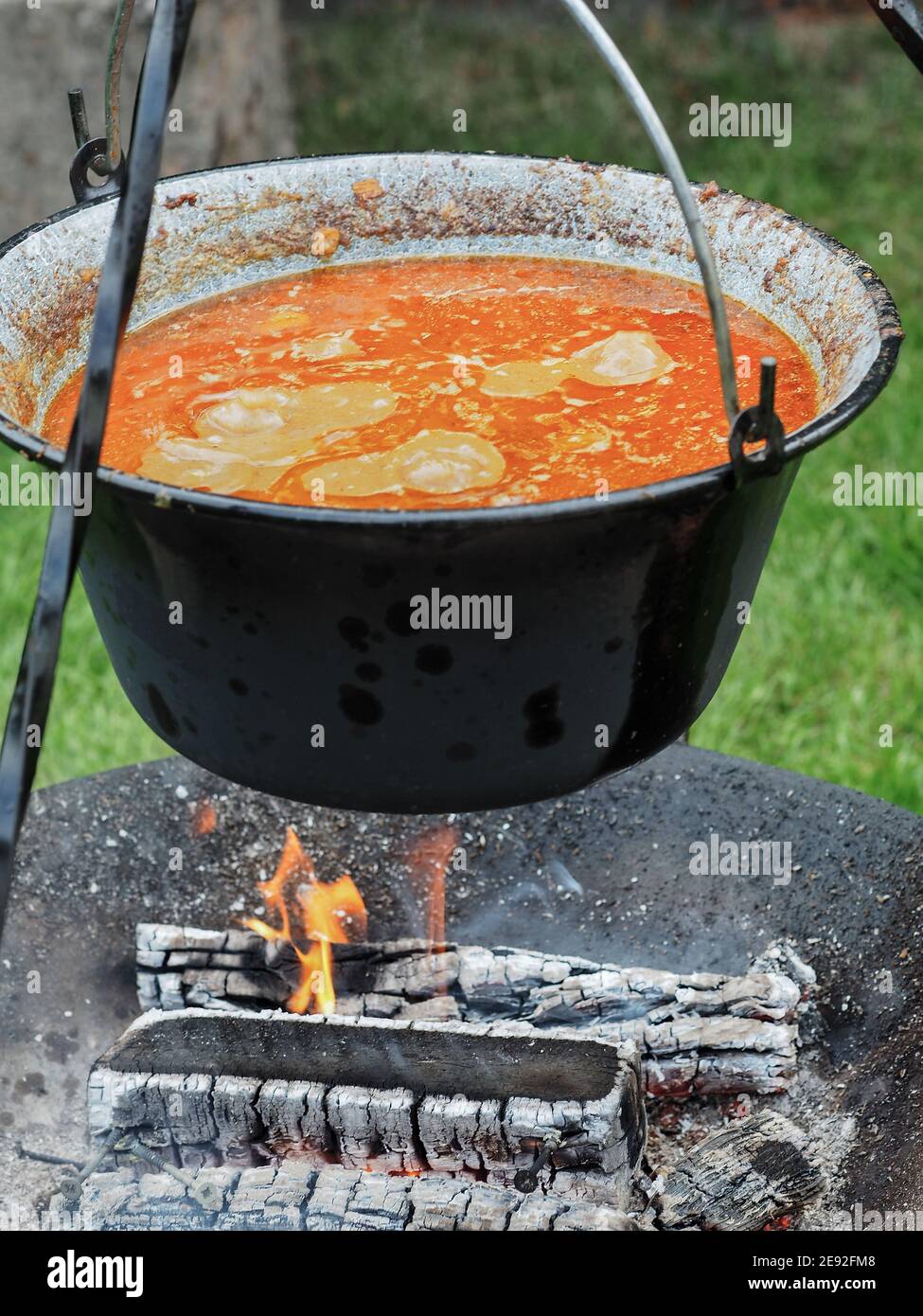 Kessel mit Gulasch auf Stativ über Kamin auf grünem Gras. Nahaufnahme. Gartenparty. Stockfoto