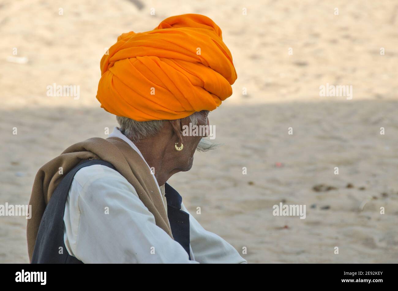 In der Morgensonne sitzt ein Kamelführer auf dem Messegelände. Der orangefarbene Turban auf seinem Kopf ist hell und attraktiv. Stockfoto