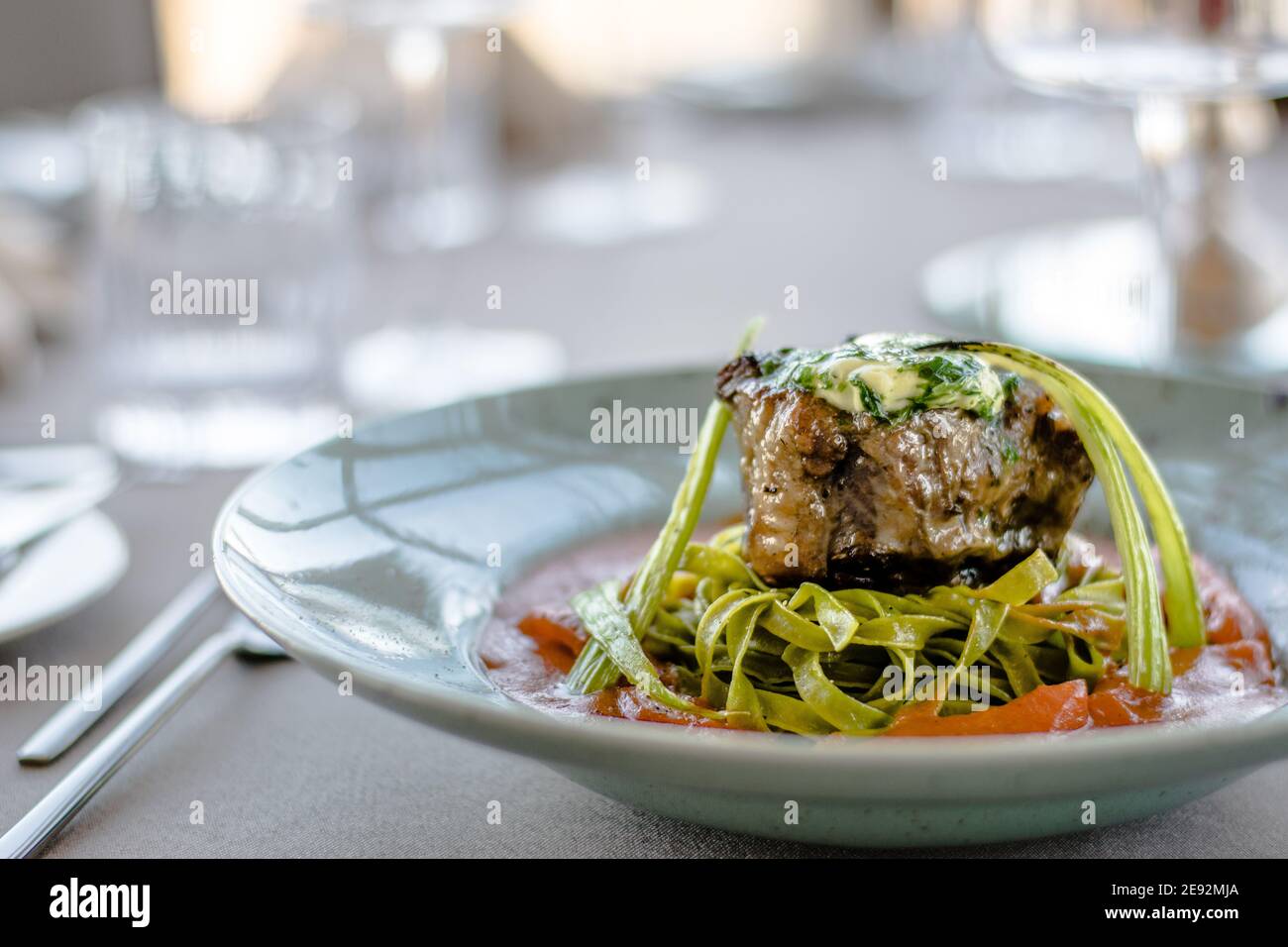 Gegrilltes und geflammtes Ochsensteak mit grünen Kräuternudeln Ein Tomatenpüree in einem Restaurant Stockfoto