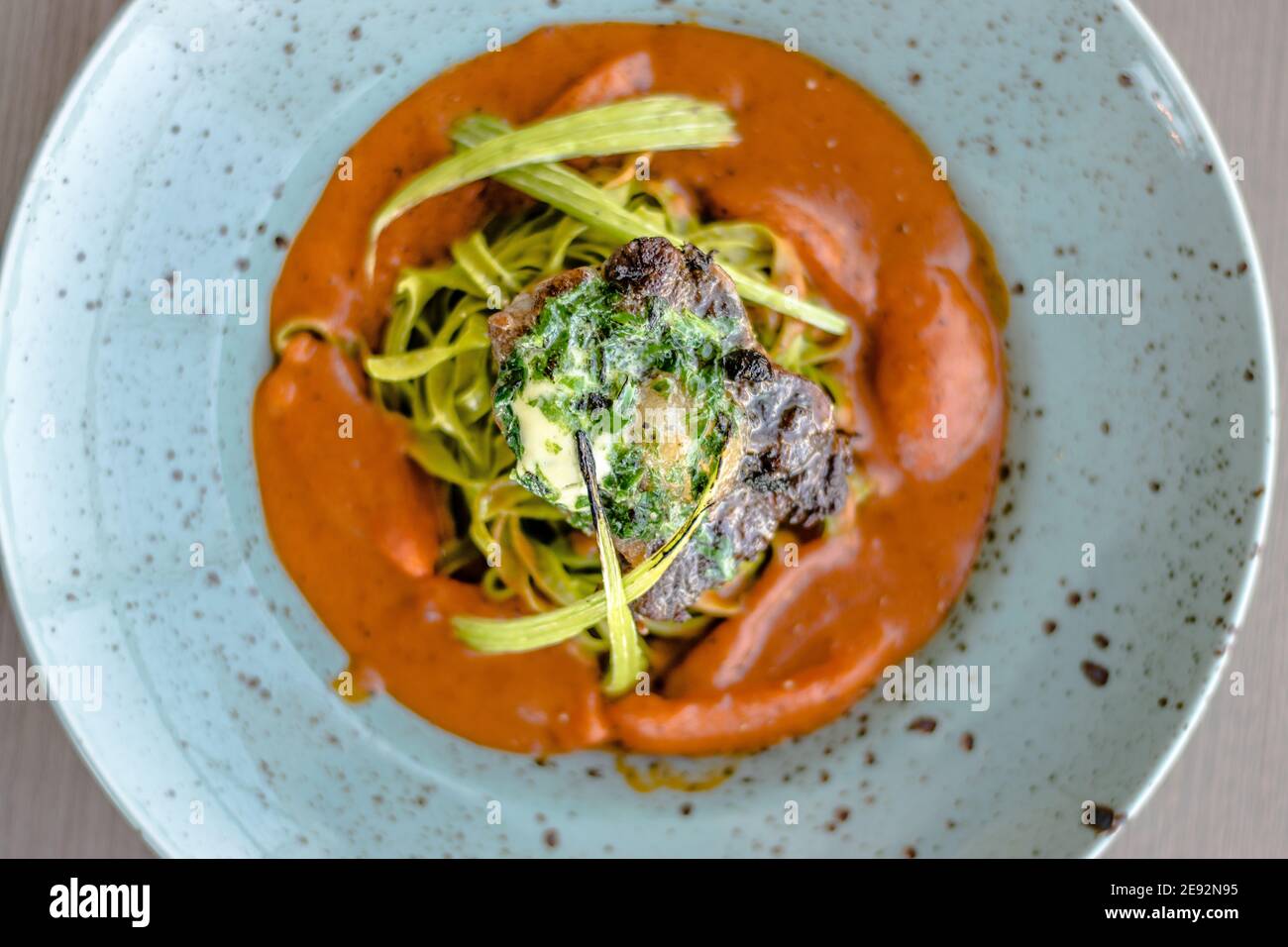 Gegrilltes und geflammtes Ochsensteak mit grünen Kräuternudeln Ein Tomatenpüree in einem Restaurant Stockfoto